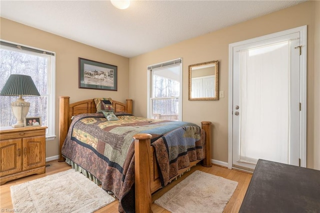 bedroom featuring multiple windows, a textured ceiling, baseboards, and light wood-style floors