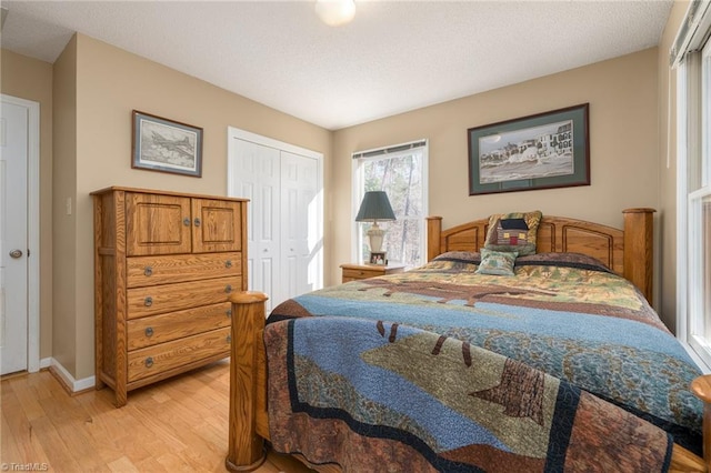 bedroom with light wood-type flooring, baseboards, a textured ceiling, and a closet