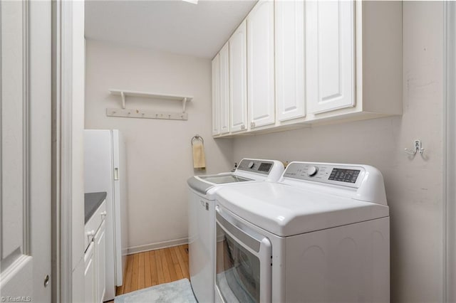 clothes washing area with cabinet space, washer and dryer, baseboards, and light wood-style floors