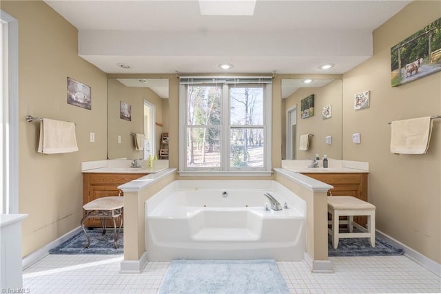 bathroom with a tub with jets, baseboards, two vanities, recessed lighting, and a sink