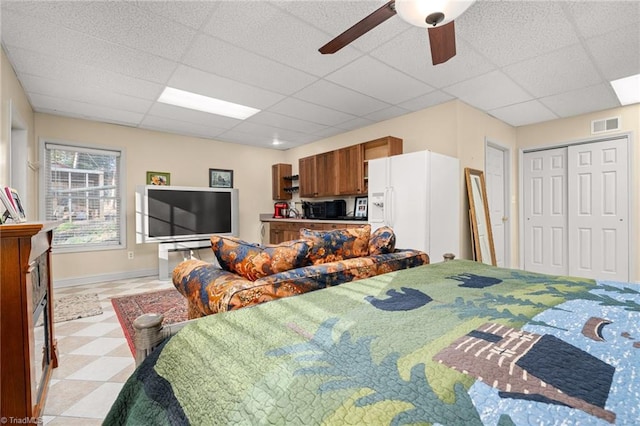 bedroom with visible vents, a ceiling fan, white fridge with ice dispenser, a paneled ceiling, and light floors