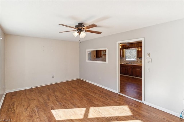 unfurnished room with a ceiling fan, a sink, baseboards, and wood finished floors