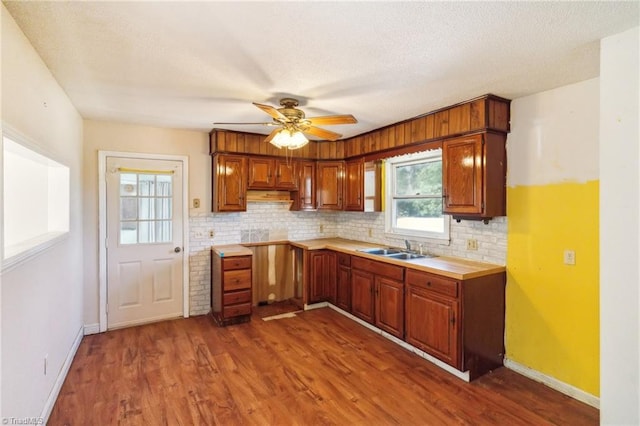 kitchen with tasteful backsplash, dark wood finished floors, brown cabinets, light countertops, and a sink