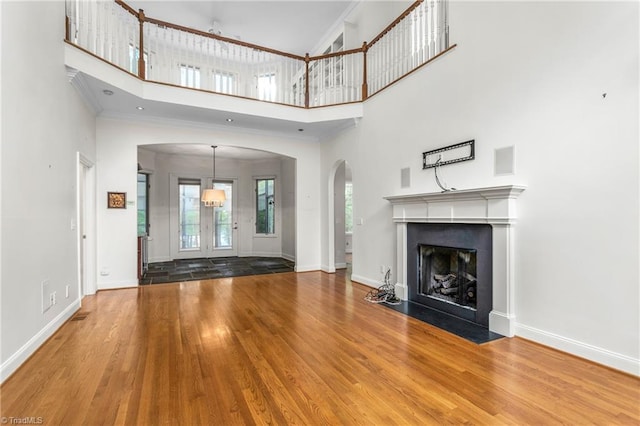 unfurnished living room with wood finished floors, a fireplace with flush hearth, arched walkways, baseboards, and a high ceiling