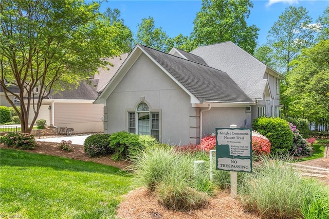 view of side of home with a lawn, a shingled roof, and stucco siding