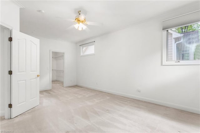 unfurnished bedroom with baseboards, light colored carpet, ornamental molding, ceiling fan, and a walk in closet