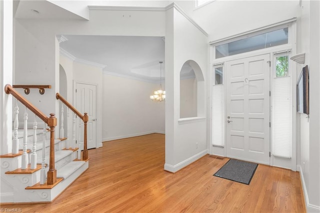 entrance foyer with baseboards, a chandelier, light wood-style floors, stairs, and crown molding