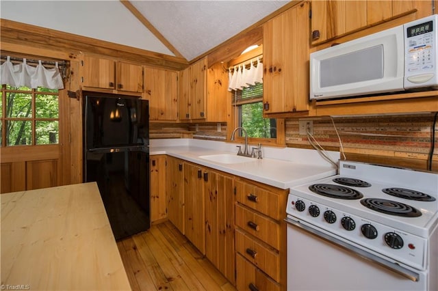 kitchen with lofted ceiling, white appliances, a sink, light countertops, and light wood finished floors