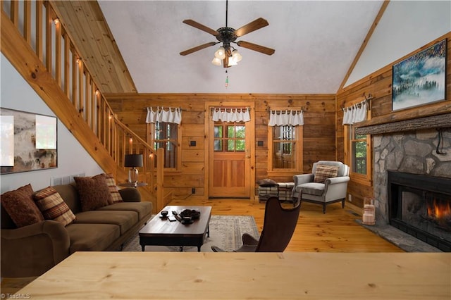 living room with wood walls, high vaulted ceiling, ceiling fan, a fireplace, and wood-type flooring