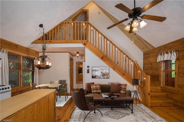 living room with a textured ceiling, light hardwood / wood-style flooring, high vaulted ceiling, and ceiling fan with notable chandelier