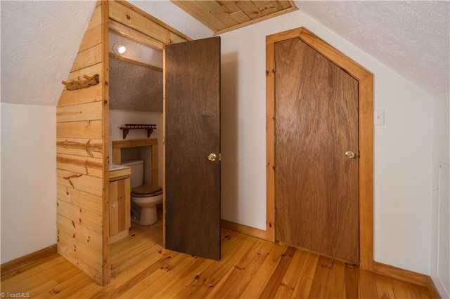 interior space featuring a textured ceiling, toilet, vaulted ceiling, and hardwood / wood-style flooring