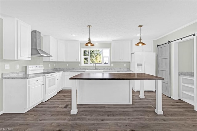 kitchen featuring a barn door, wall chimney range hood, white appliances, a kitchen island, and white cabinetry