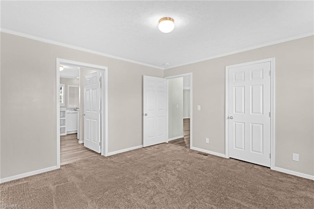 unfurnished bedroom with a textured ceiling, ensuite bathroom, crown molding, and carpet flooring