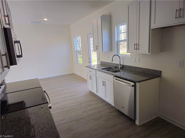 kitchen featuring dark stone counters, white cabinetry, stainless steel appliances, hardwood / wood-style floors, and sink