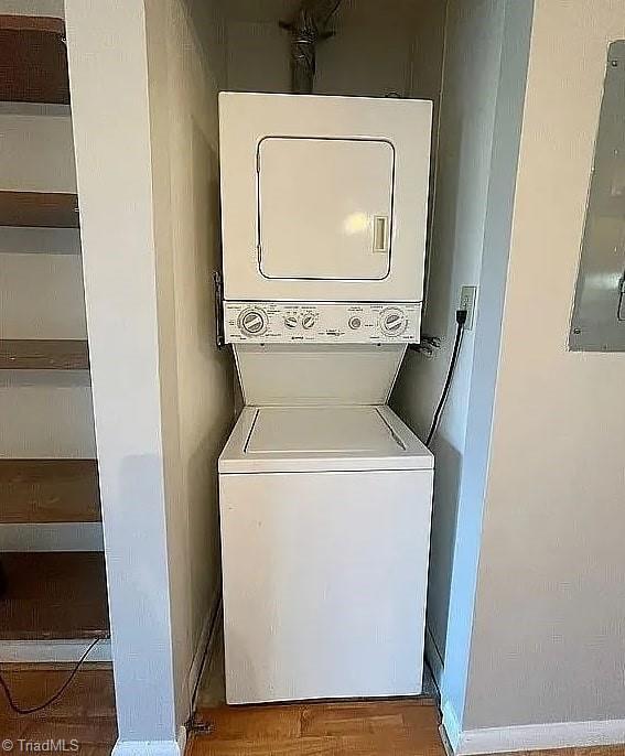 laundry room featuring stacked washer / drying machine, hardwood / wood-style flooring, and electric panel