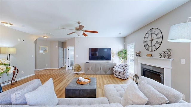 living room featuring wood finished floors, visible vents, baseboards, ceiling fan, and a glass covered fireplace