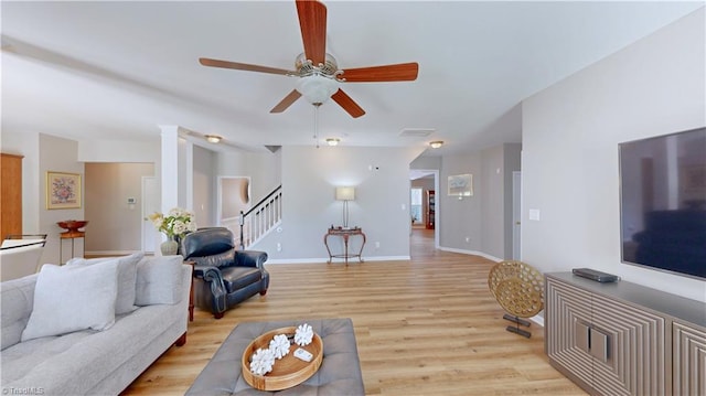 living room with visible vents, baseboards, stairway, light wood-style floors, and a ceiling fan