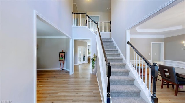 staircase with crown molding, wood finished floors, baseboards, and a towering ceiling