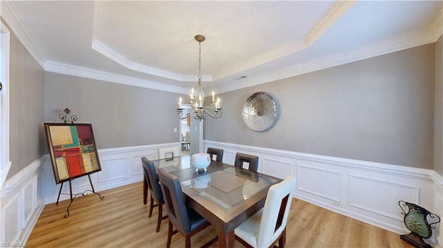 dining area featuring a tray ceiling, a notable chandelier, a wainscoted wall, and light wood finished floors