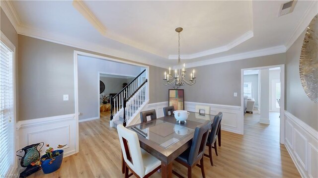 dining space with a raised ceiling, a notable chandelier, light hardwood / wood-style flooring, and ornamental molding