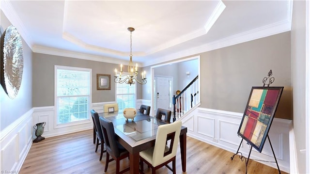 dining area with a raised ceiling, stairway, a notable chandelier, and light wood-type flooring