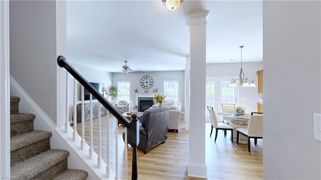 stairs with ceiling fan with notable chandelier, decorative columns, wood finished floors, and a healthy amount of sunlight