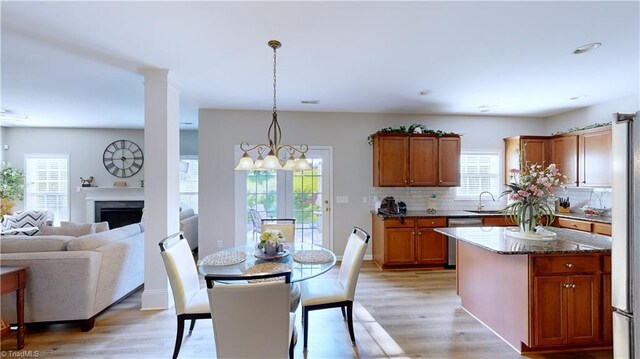 kitchen with dishwasher, light hardwood / wood-style floors, decorative backsplash, an inviting chandelier, and dark stone counters