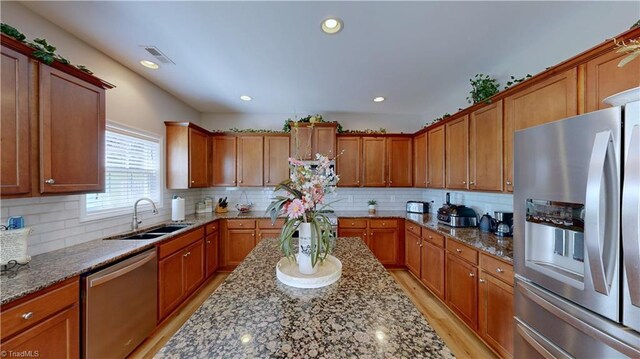 kitchen with stainless steel appliances, light hardwood / wood-style flooring, decorative backsplash, sink, and light stone counters