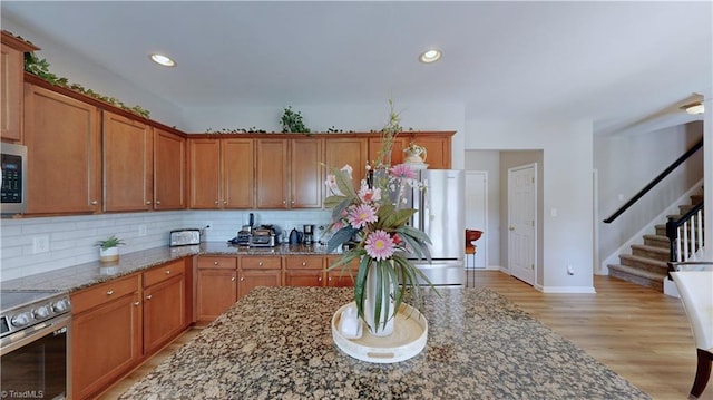 kitchen with dark stone countertops, appliances with stainless steel finishes, and brown cabinetry