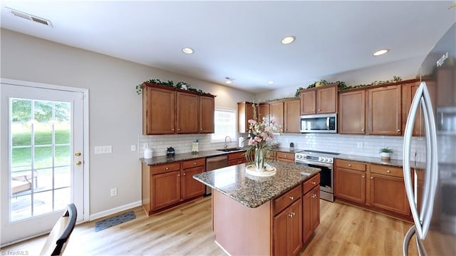 kitchen with sink, light wood-type flooring, tasteful backsplash, a kitchen island, and stainless steel appliances