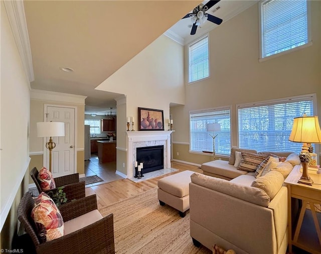 living room with a high end fireplace, light wood-type flooring, ceiling fan, ornamental molding, and a high ceiling