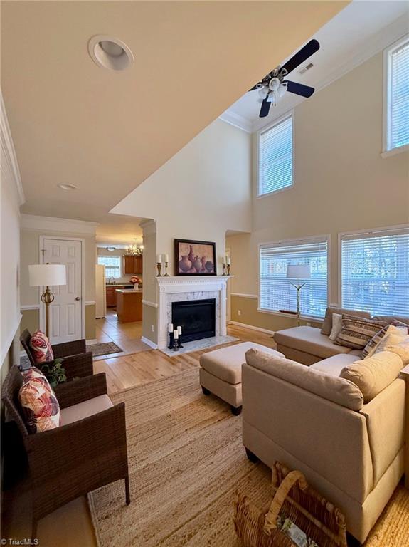 living room with a premium fireplace, a towering ceiling, crown molding, light hardwood / wood-style flooring, and ceiling fan with notable chandelier