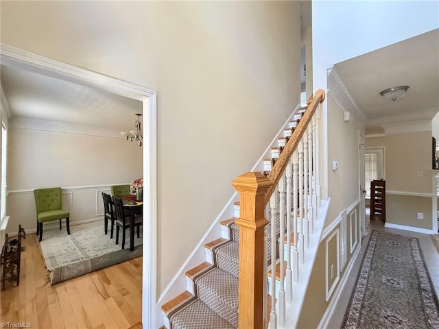 stairs with crown molding, hardwood / wood-style flooring, and a notable chandelier