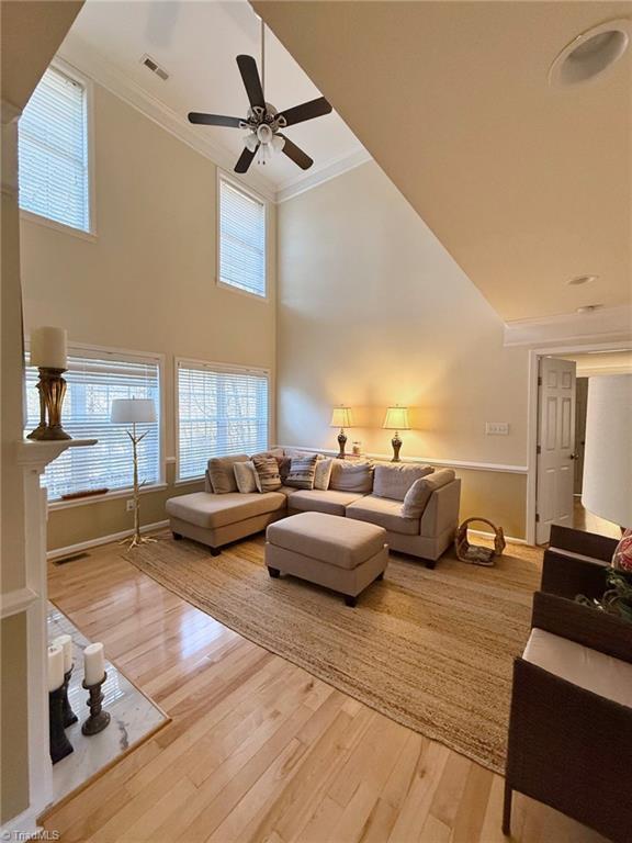 living room with a towering ceiling, ornamental molding, ceiling fan, and wood-type flooring