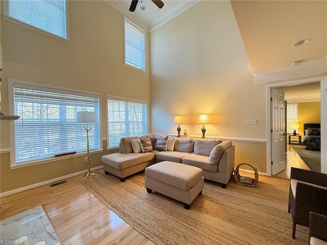 living room featuring a towering ceiling, ceiling fan, crown molding, and light hardwood / wood-style flooring