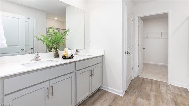 full bathroom featuring a sink, baseboards, double vanity, and wood finished floors
