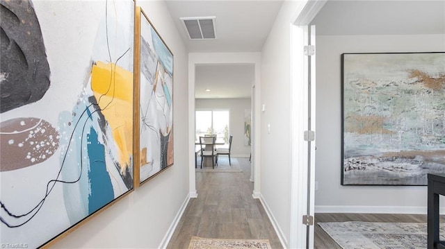 hallway with visible vents, baseboards, and wood finished floors