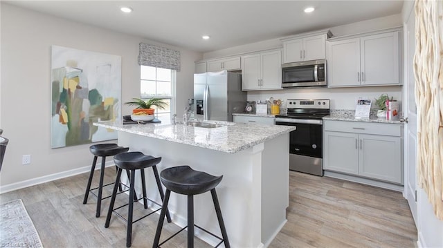kitchen with a sink, light wood finished floors, a breakfast bar area, and stainless steel appliances