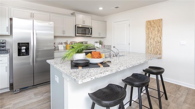 kitchen featuring visible vents, light stone countertops, a breakfast bar, light wood-type flooring, and stainless steel appliances