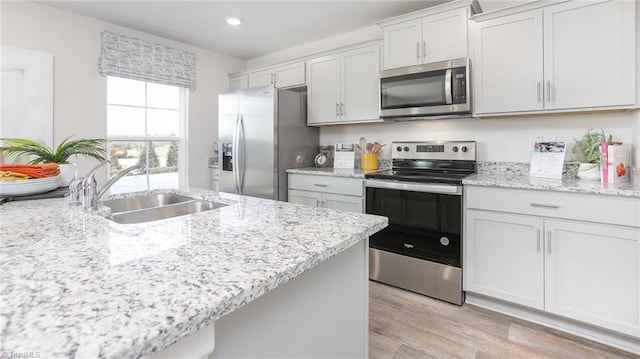kitchen featuring light stone countertops, appliances with stainless steel finishes, a sink, light wood-style flooring, and recessed lighting