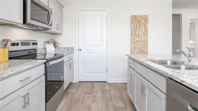 kitchen featuring a sink, light stone counters, light wood-style floors, and stainless steel appliances
