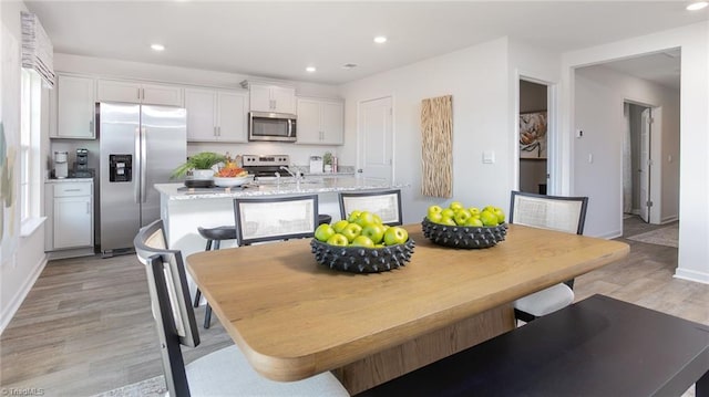 interior space with a center island with sink, recessed lighting, white cabinets, light wood finished floors, and stainless steel appliances