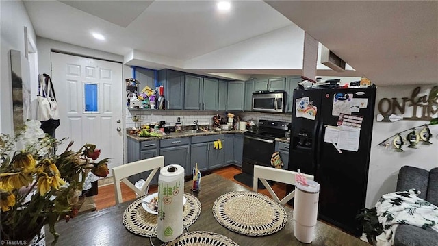 kitchen featuring tasteful backsplash, vaulted ceiling, dark wood-type flooring, and black appliances