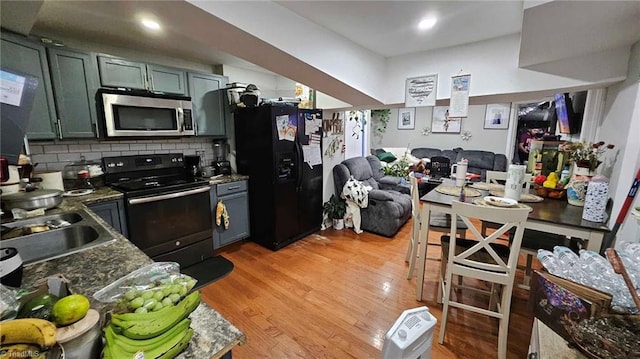 kitchen with tasteful backsplash, sink, dark stone countertops, black appliances, and light hardwood / wood-style flooring