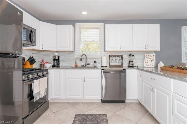 kitchen featuring appliances with stainless steel finishes, a sink, decorative backsplash, light stone countertops, and white cabinetry