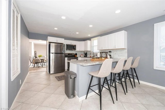 kitchen featuring stainless steel appliances, a peninsula, backsplash, white cabinetry, and a kitchen bar