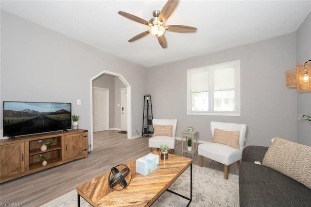 living room with ceiling fan, light wood-style floors, arched walkways, and baseboards