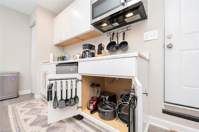 detailed view of stainless steel microwave, white cabinetry, baseboards, and light wood finished floors