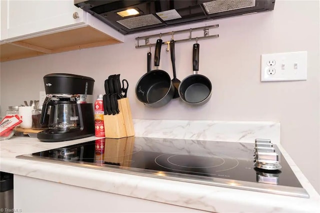 kitchen view of black electric cooktop, extractor fan, white cabinets, and light countertops