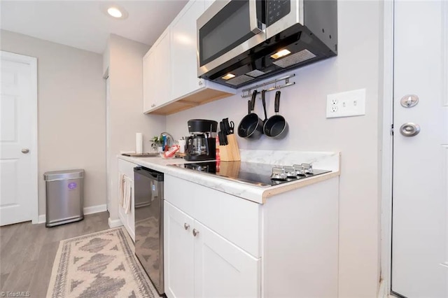 kitchen with appliances with stainless steel finishes, white cabinetry, a sink, light countertops, and light wood finished floors